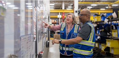 Image of two employees looking at a board on a wall.