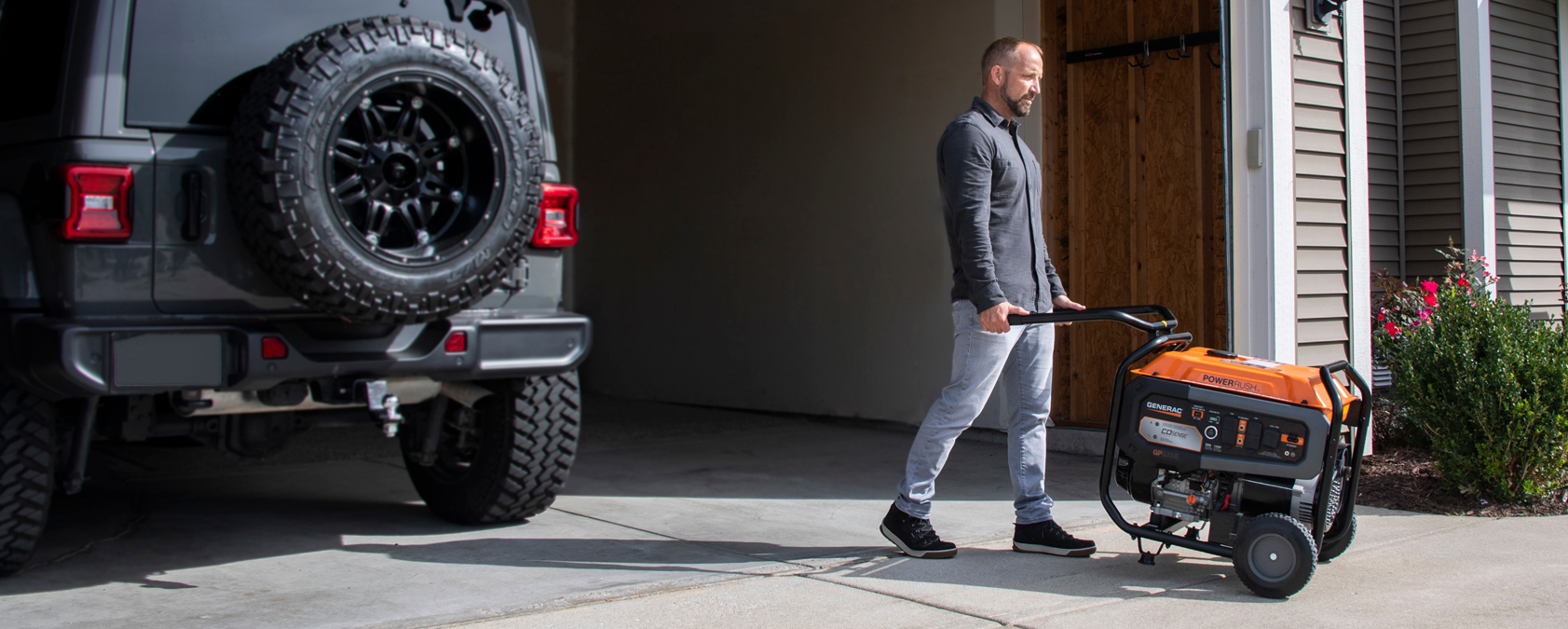 Person wheeling a Generac portable generator out of a garage