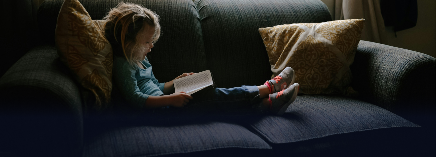 Child reading a book on the couch using light from window