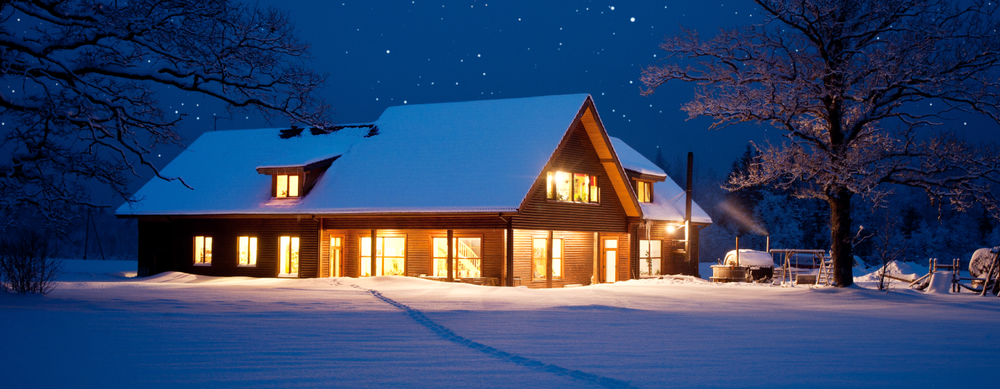 log home with lights on surrounded in snow on a starry night