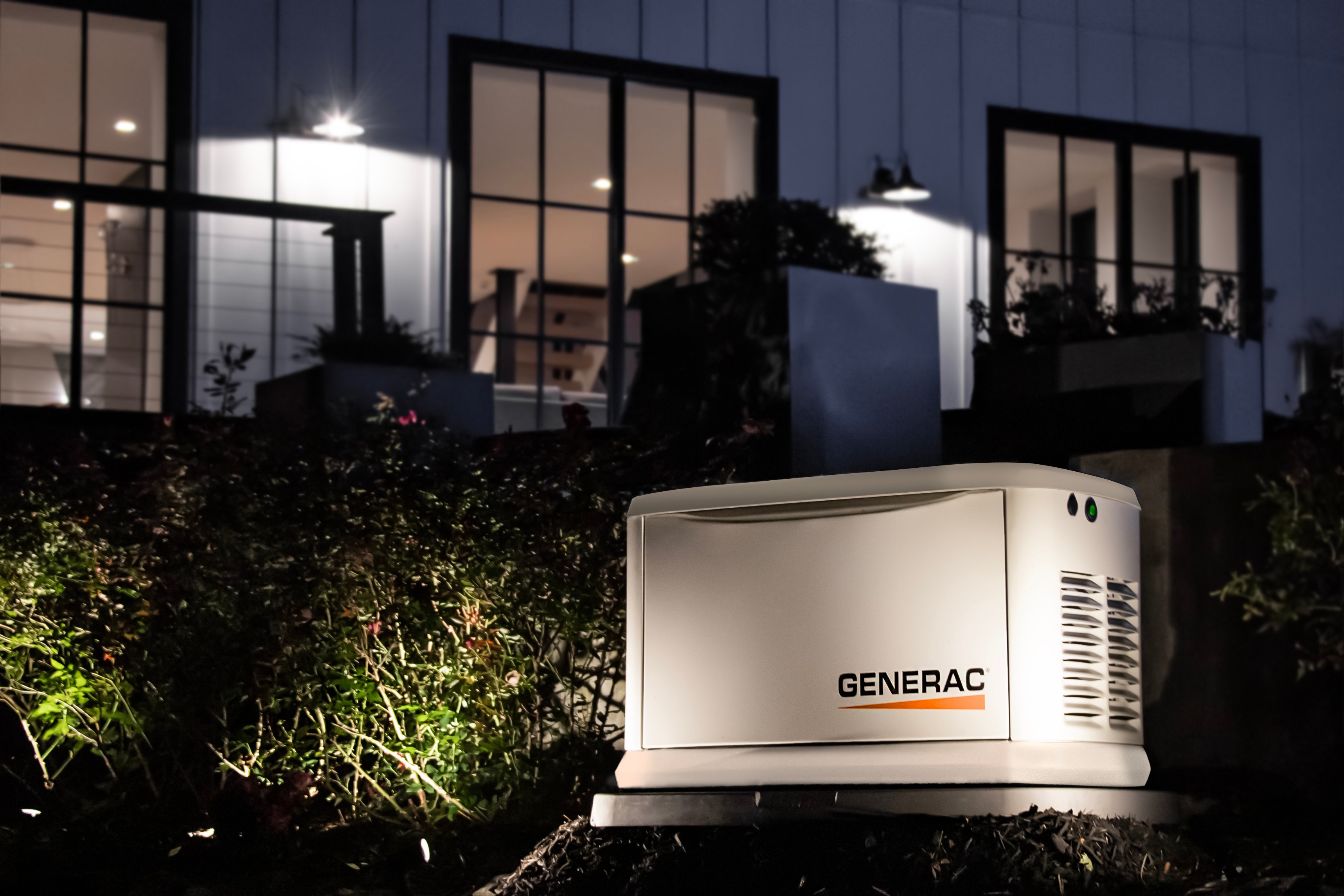 Generac Home Standby Backup Generator lit up behind a house at night.